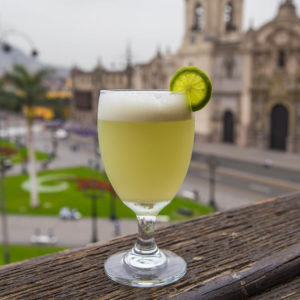 Traditional pisco sour drink with a view of Lima's Plaza de Armas in the background