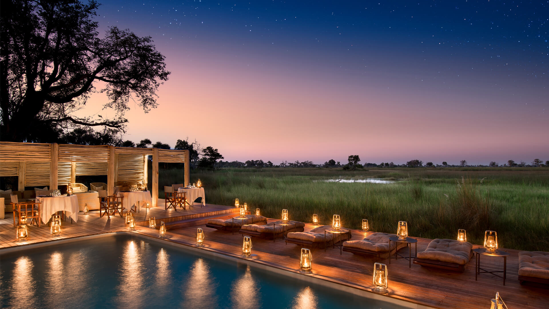 Private dinner tables and lanterns around pool with starry sky above