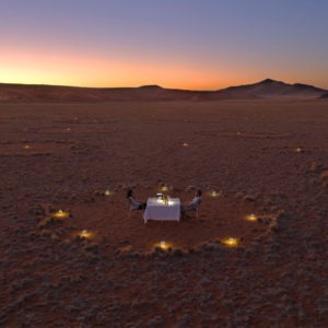 A couple sits at their dinner for two in the middle of a fairy circle in the Namib Desert